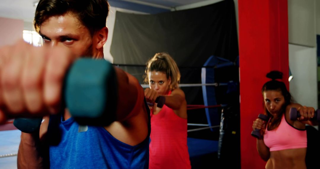 Intense Group Boxing Workout Reaching Forward with Dumbbells, Focused Gym Training