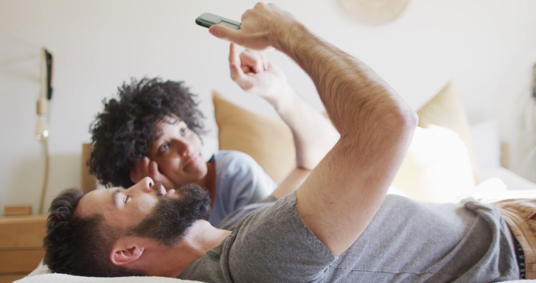 Image of happy diverse couple relaxing at home, lying on bed using smartphone - Free Images, Stock Photos and Pictures on Pikwizard.com