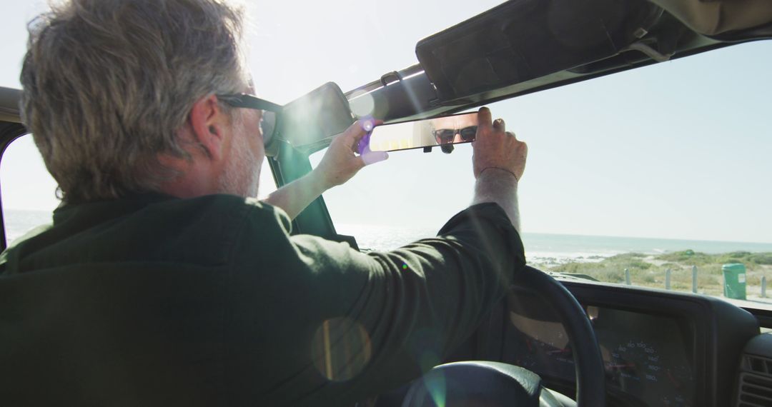 Man Adjusting Rearview Mirror While Driving Coastal Road - Free Images, Stock Photos and Pictures on Pikwizard.com