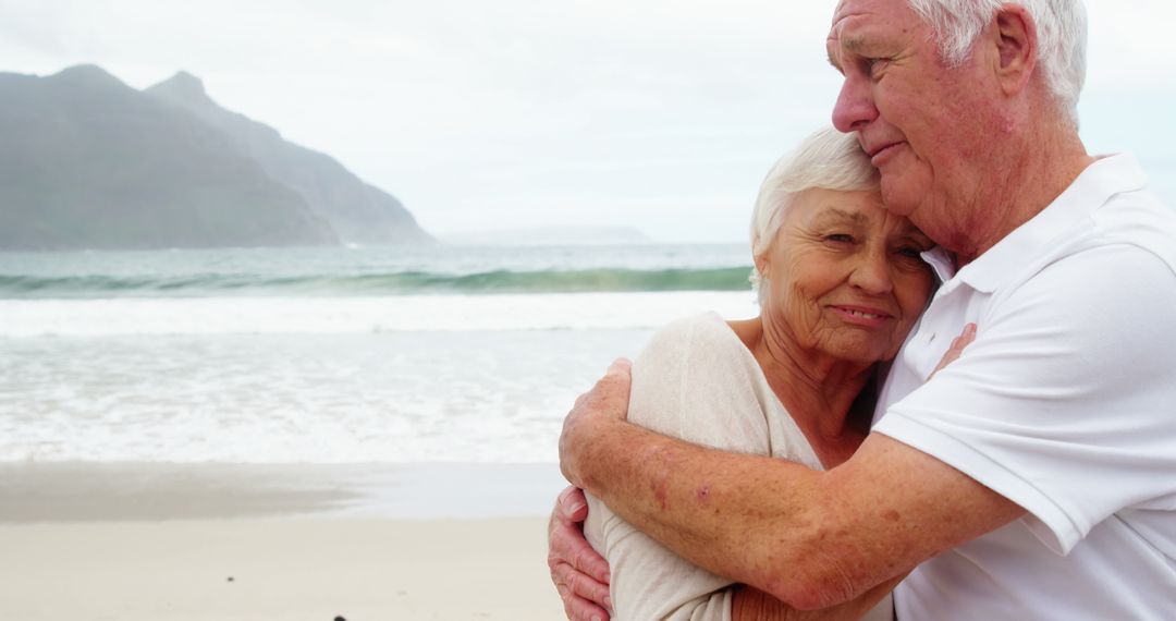 Senior Couple Embracing on Beach with Mountain in Background - Free Images, Stock Photos and Pictures on Pikwizard.com