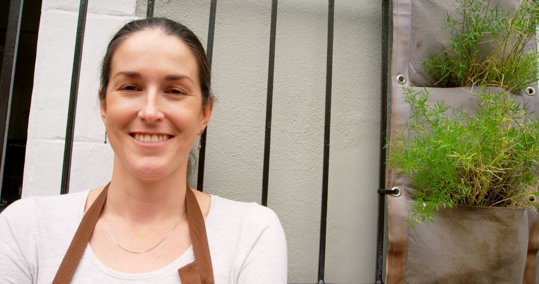 Smiling Woman with Apron Next to Vertical Garden - Free Images, Stock Photos and Pictures on Pikwizard.com