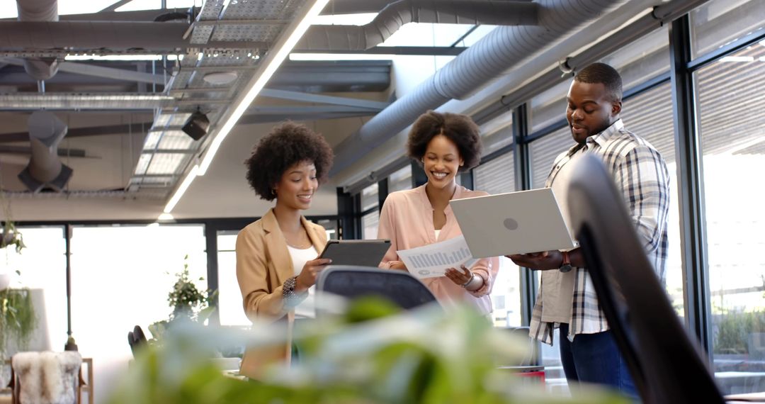 Smiling professionals collaborating with laptop and tablet in modern open-plan office