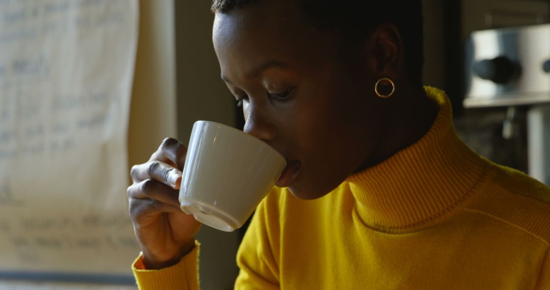 Woman Enjoying Coffee Wearing Yellow Sweater by Cozy Window - Free Images, Stock Photos and Pictures on Pikwizard.com