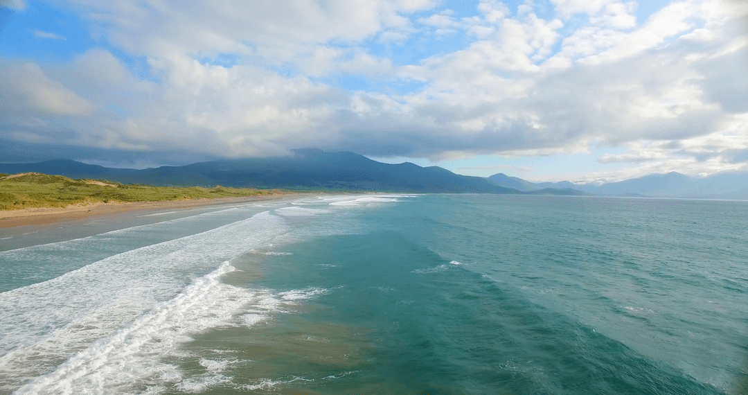 Idyllic Transparent Ocean Waves Meet Lush Coastline Under Dramatic Sky