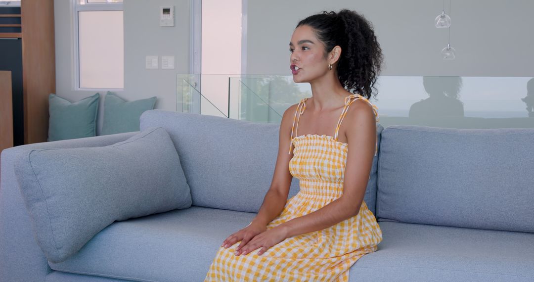 Young woman sitting on sofa indoors wearing yellow checkered dress