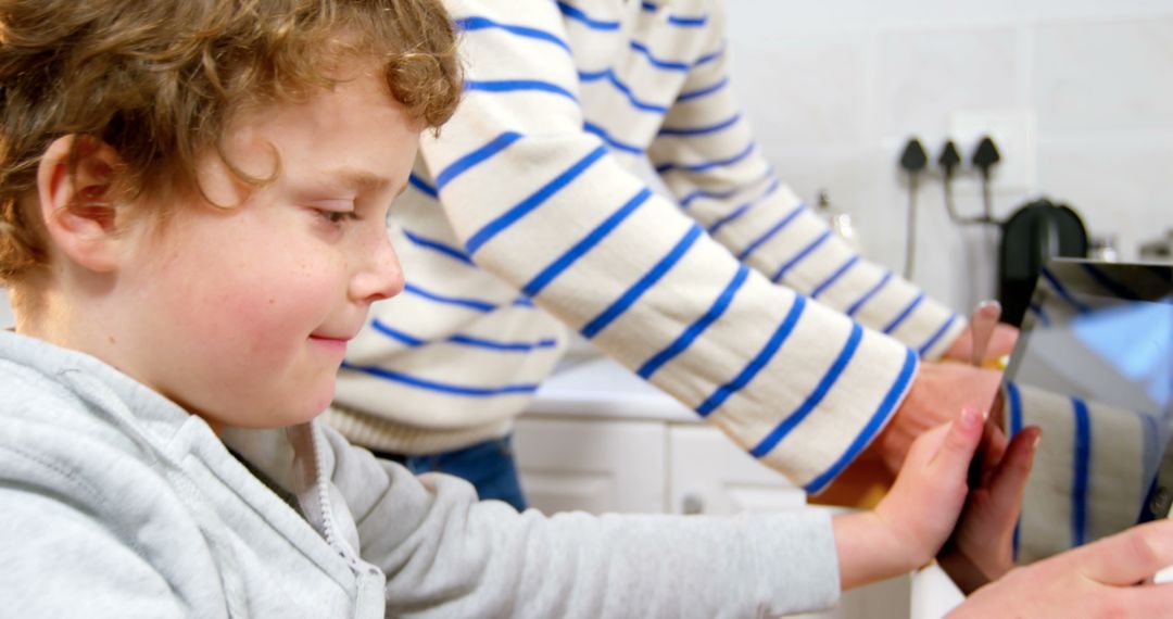 Curly-haired child learning to wash hands with touchscreen guidance in kitchen - Free Images, Stock Photos and Pictures on Pikwizard.com