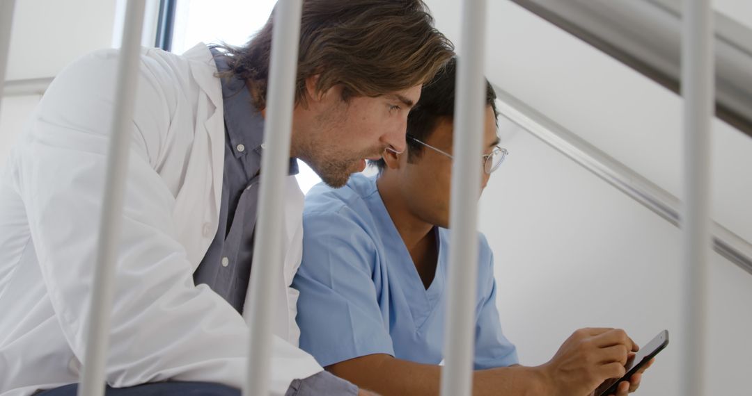 Male Doctors Collaborating on Smartphone in Hospital Corridor - Free Images, Stock Photos and Pictures on Pikwizard.com