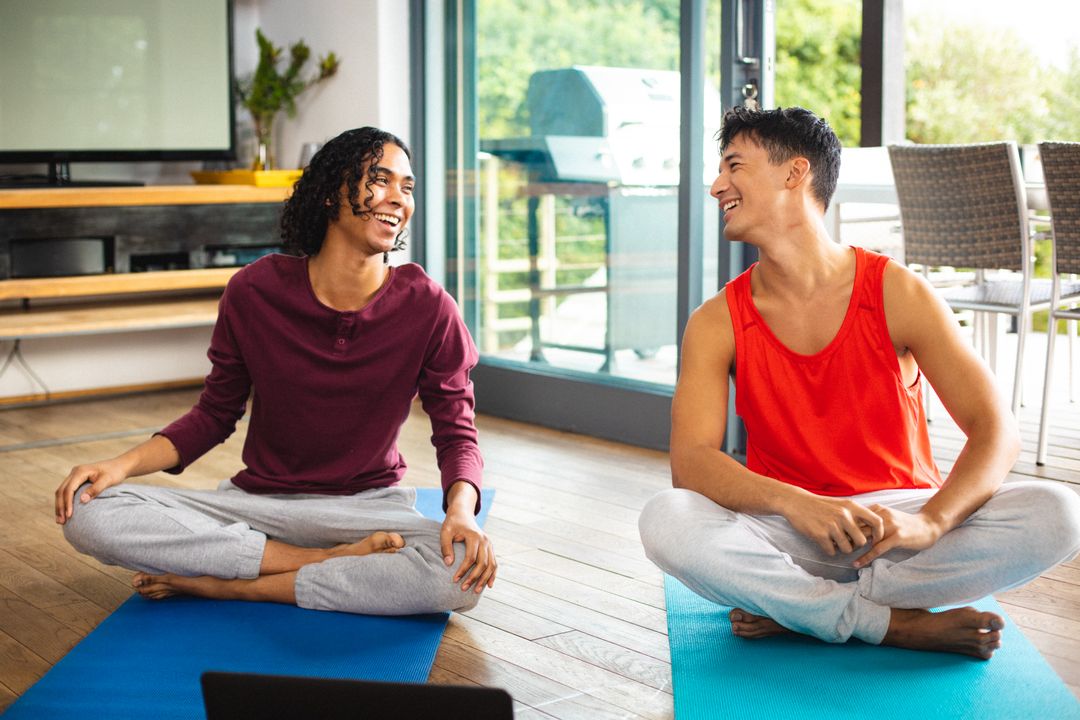 Multiracial gay couple looking at each other and laughing while meditating on mats at home - Free Images, Stock Photos and Pictures on Pikwizard.com