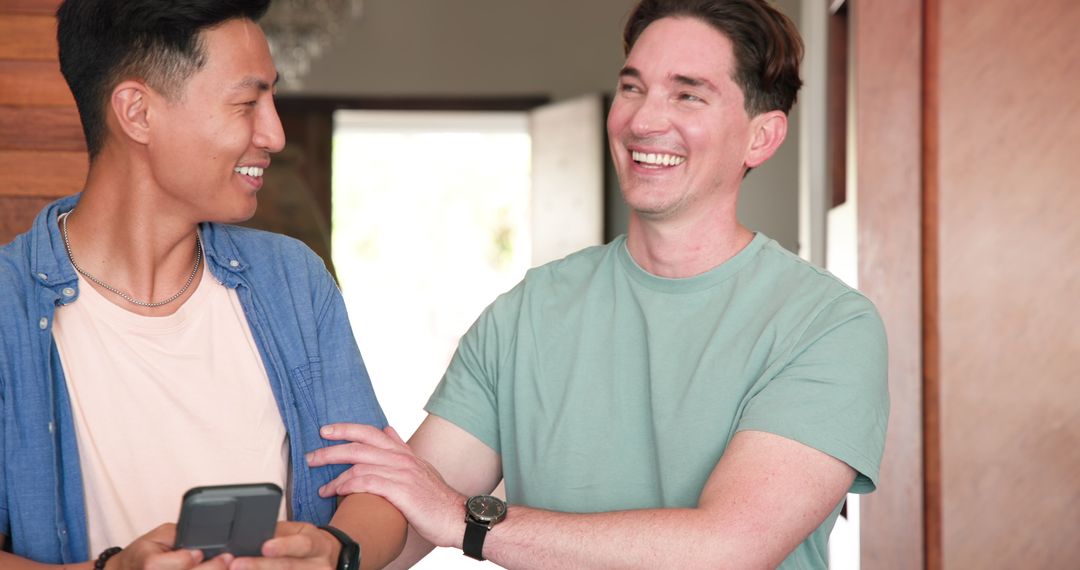 Diverse Male Couple Laughing While Engaging with Smartphone