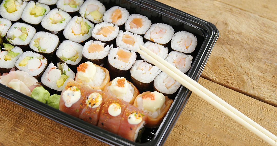 Assorted Sushi Rolls in Takeout Container with Chopsticks on Wooden Table - Free Images, Stock Photos and Pictures on Pikwizard.com