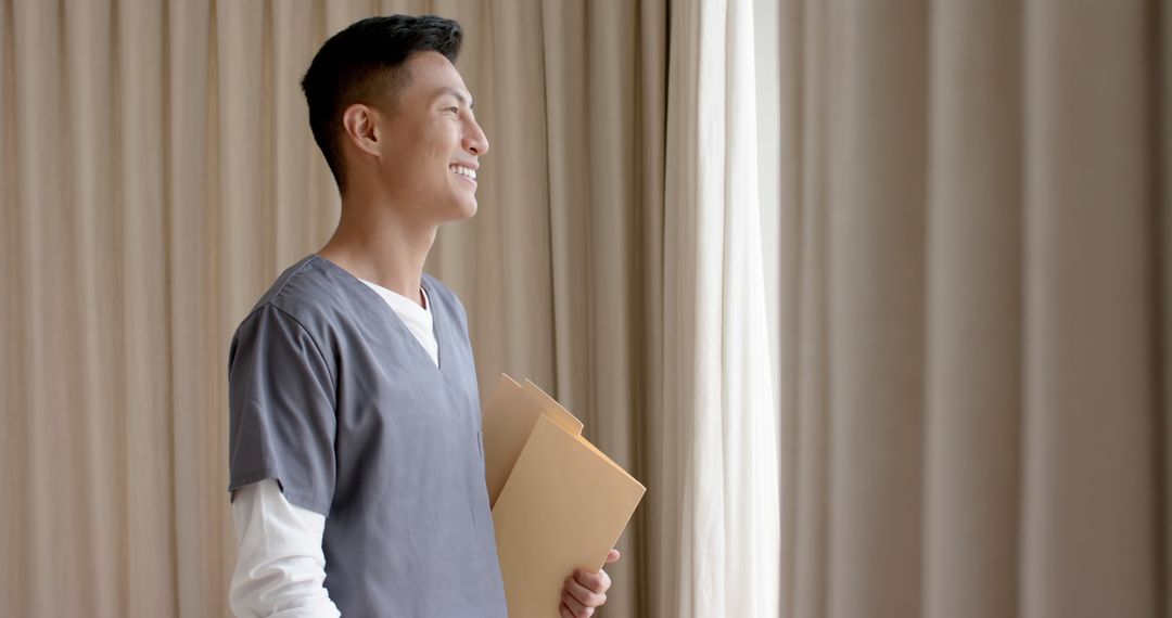 Smiling Asian Doctor Holding Patient Files by Window