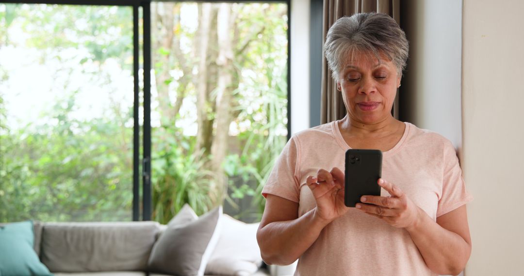 Senior Woman Relaxing with Smartphone Near Sunny Window at Home