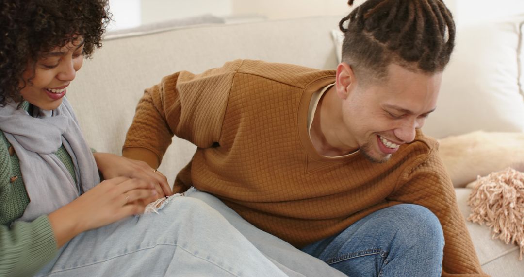 Laughing couple cuddling on sofa in cozy knit sweaters and jeans, intimate home moment