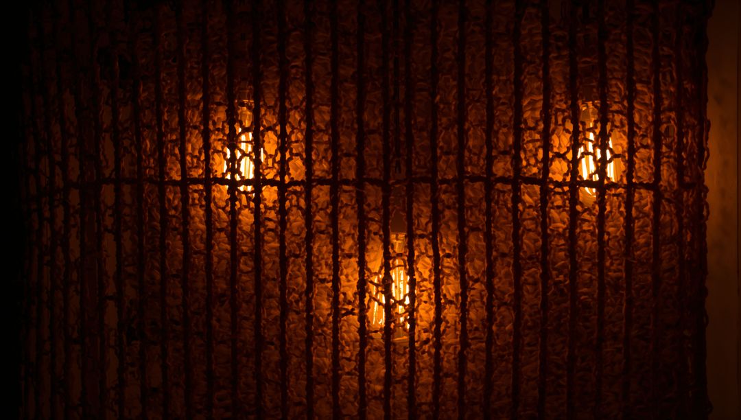 Woven lattice backlighting creating amber glow and textured shadows with filament bulbs