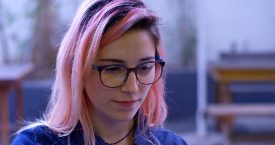 Young woman with pink hair and glasses focused on work - Free Images, Stock Photos and Pictures on Pikwizard.com