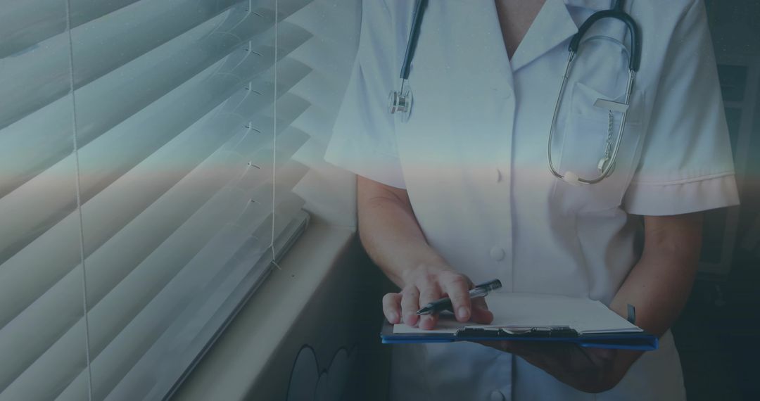 Nurse writing patient notes by window with stethoscope and clipboard in clinic
