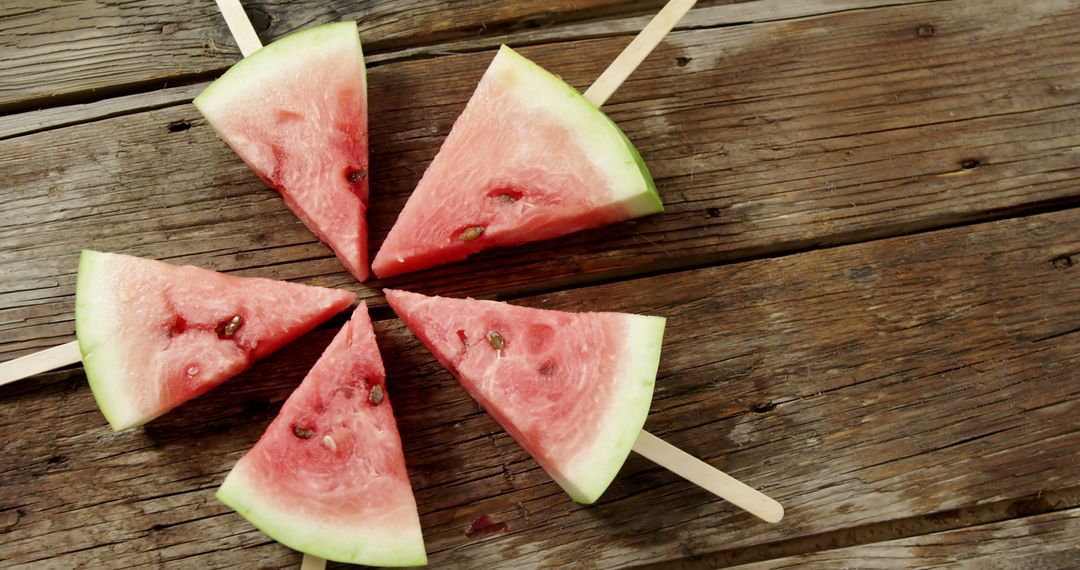 Slices of watermelon on popsicle sticks are arranged in a circular pattern on a rustic wooden table - Free Images, Stock Photos and Pictures on Pikwizard.com