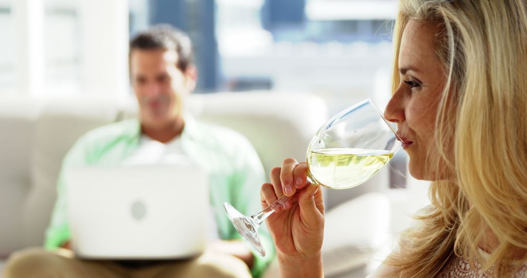Woman Enjoying White Wine While Man Works in Background at Home