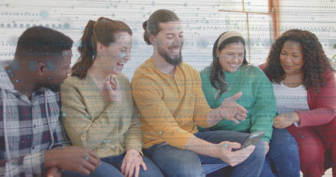 Group of five friends laughing and sharing smartphone on blue sofa, casual sweaters