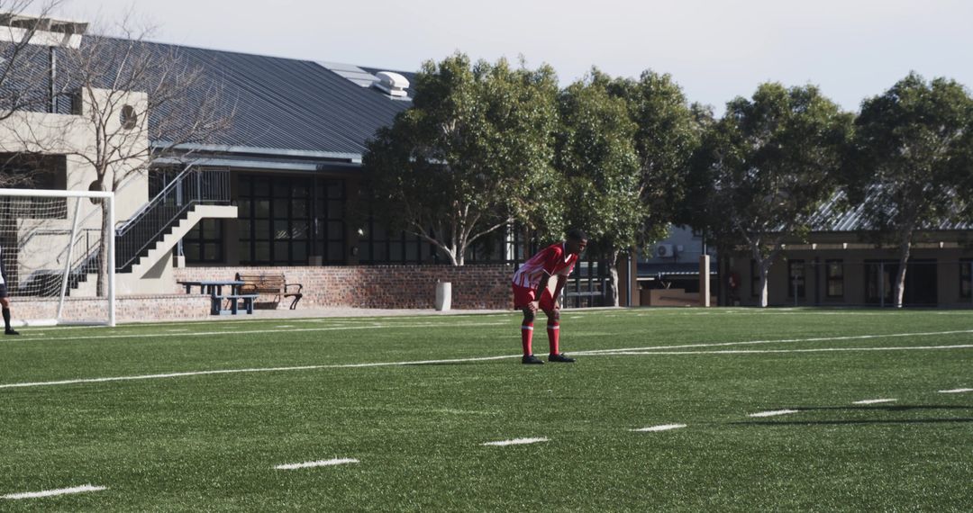 Youth Soccer Player in Red Uniform on Field near School Buildings