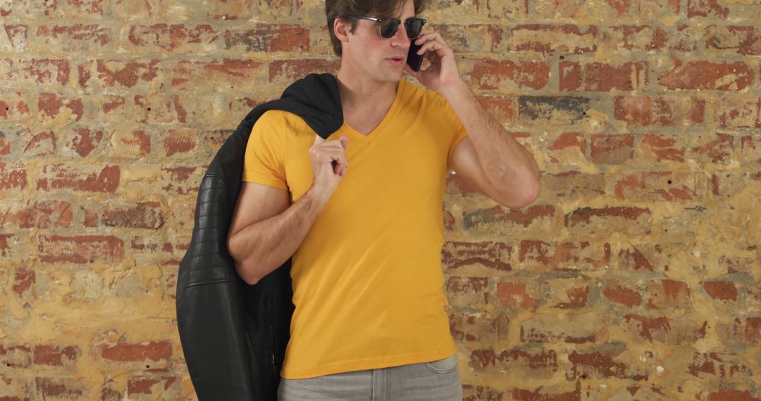 Fashionable Man Wearing Sunglasses and Talking on Phone Against Brick Wall - Free Images, Stock Photos and Pictures on Pikwizard.com