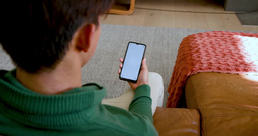 Relaxed Young Asian Man Browsing Smartphone in Modern Living Room