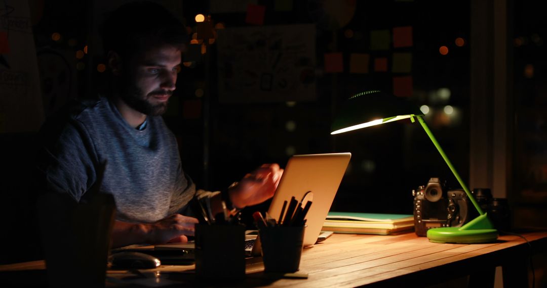 Focused Male Working Late Night at Desk with Green Lamp - Free Images, Stock Photos and Pictures on Pikwizard.com