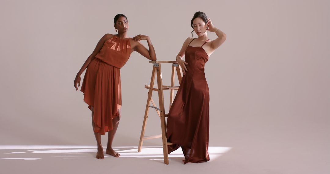 Elegant Models in Rust-Colored Satin Dresses with Studio Ladder