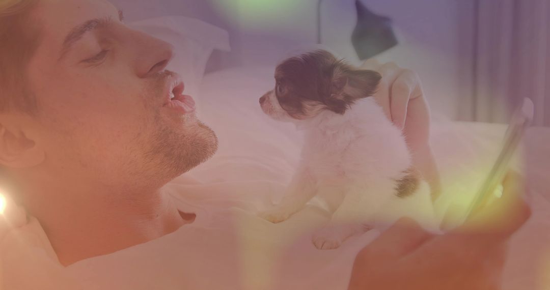 Man Relaimg in Bedroom Balancing Small Puppy and Holding Smartphone