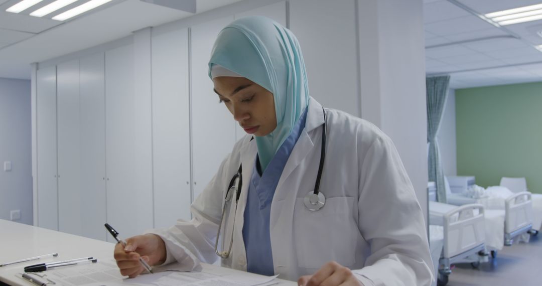 Focused Muslim Doctor Reviewing Patient Files in Hospital - Free Images, Stock Photos and Pictures on Pikwizard.com