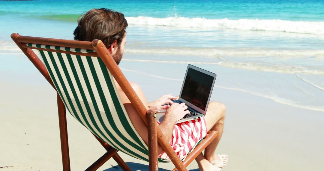 Man sitting on armchair using laptop at beach 4k - Free Images, Stock Photos and Pictures on Pikwizard.com