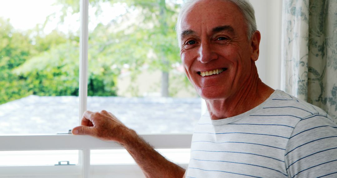 Happy Senior Man Smiling by Sunlit Window - Free Images, Stock Photos and Pictures on Pikwizard.com