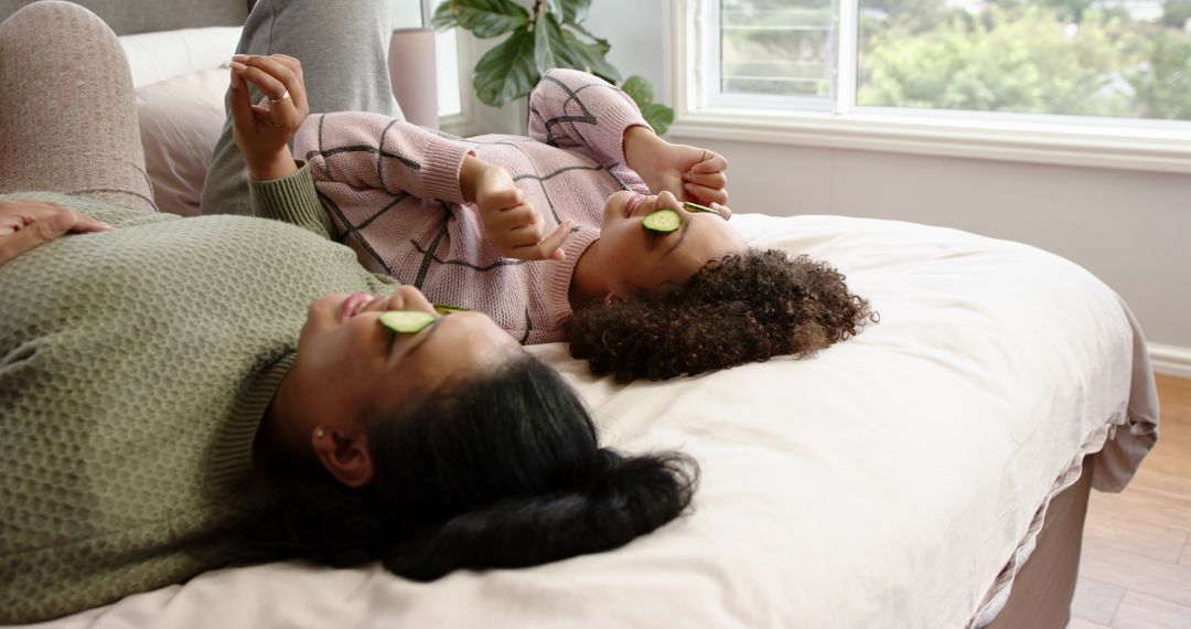 Relaxing home spa ritual with friends lying on bed using cucumber eye slices and thumbs-up