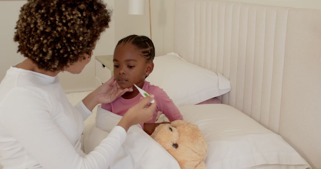 Mother Checking Daughter's Temperature as Child Hugs Teddy Bear