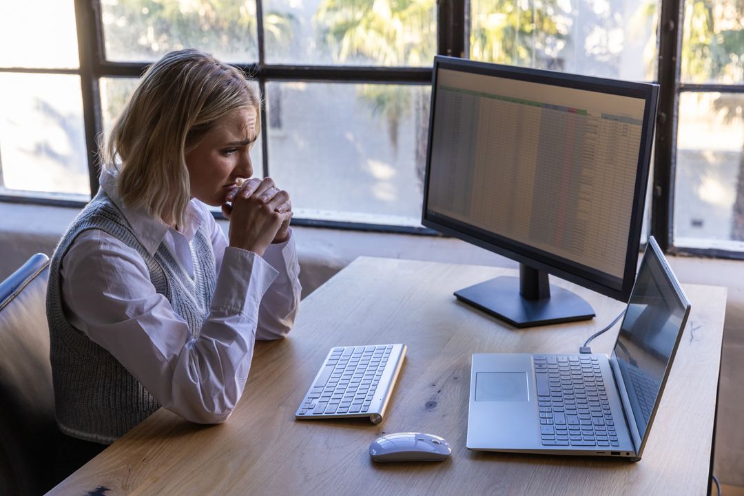 Professional Woman Analyzing Data on Dual Monitors in Sunlit Office