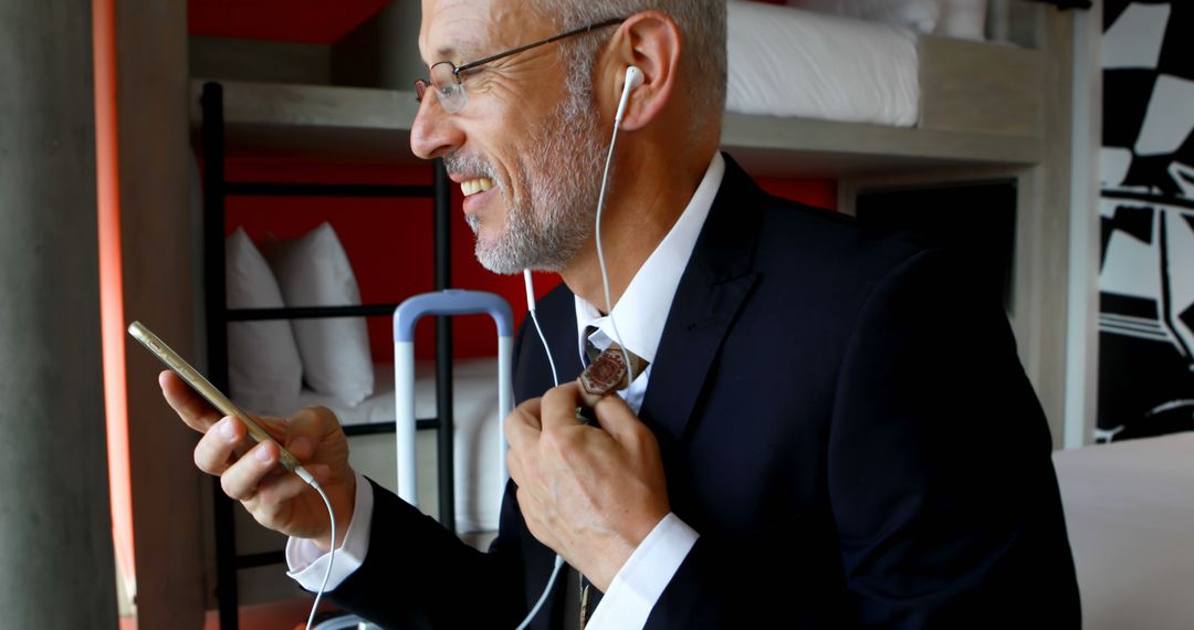 Senior Businessman Working on Smartphone with Earphones in Hotel Room - Free Images, Stock Photos and Pictures on Pikwizard.com