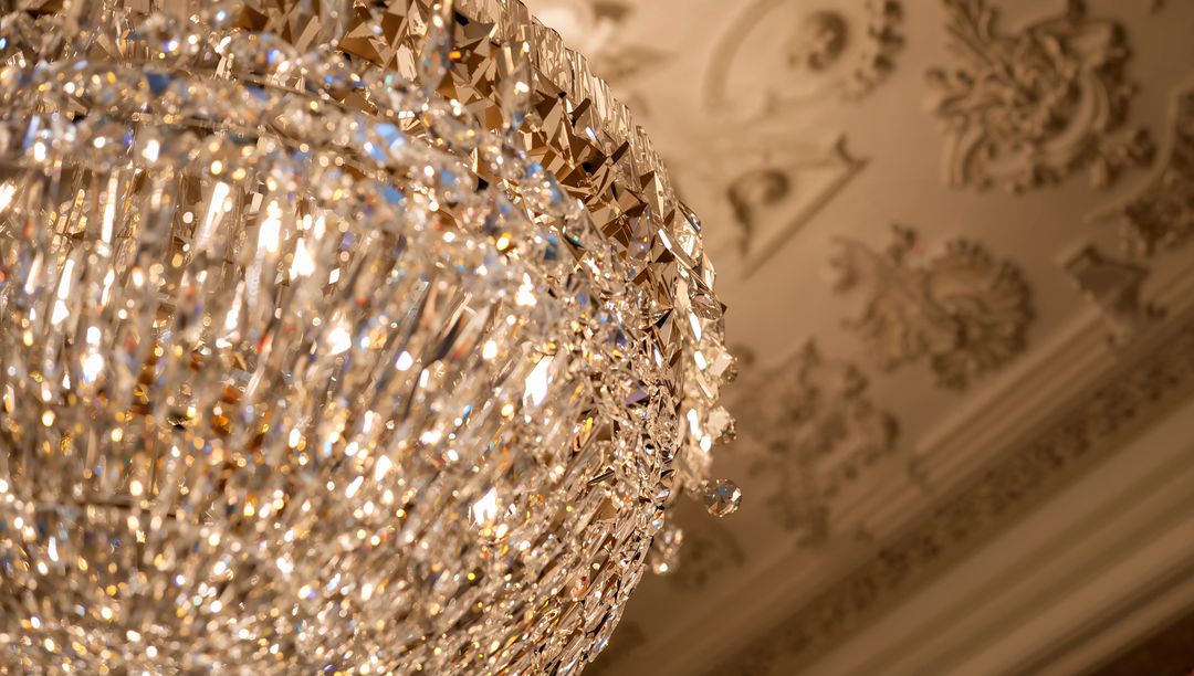 Glittering crystal chandelier illuminating ornate plaster ceiling in salon with warm bokeh