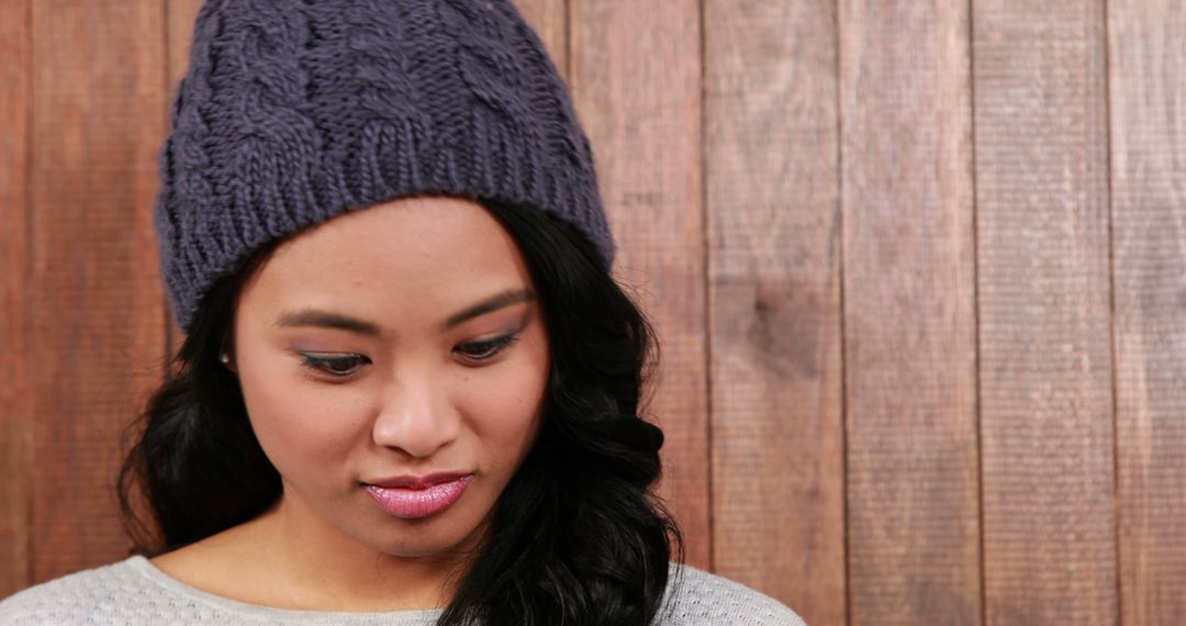 Pensive Young Woman in Knitted Beanie Standing Against Wooden Wall - Free Images, Stock Photos and Pictures on Pikwizard.com