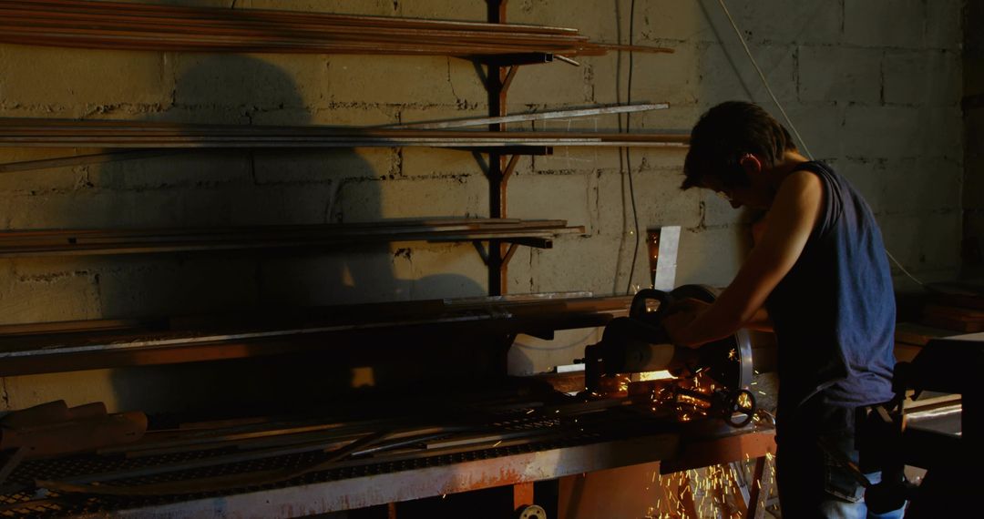 Worker grinding metal at bench with flying sparks and strong shadow in industrial workshop
