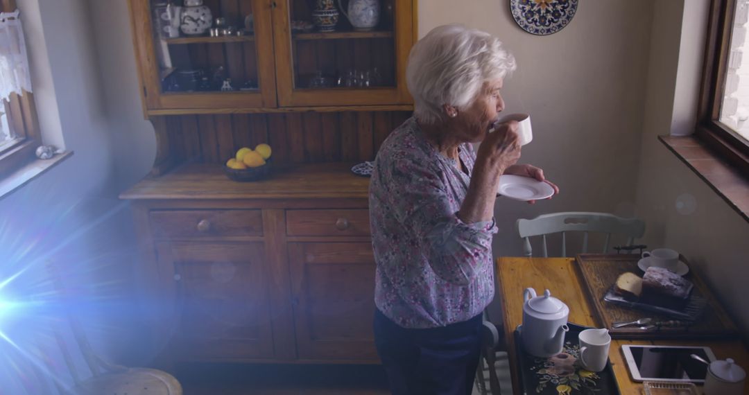 Senior woman sipping tea in sunlit kitchen
