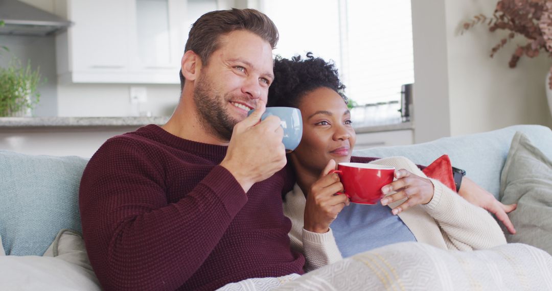 Image of happy diverse couple embracing and drinking coffee on sofa - Free Images, Stock Photos and Pictures on Pikwizard.com