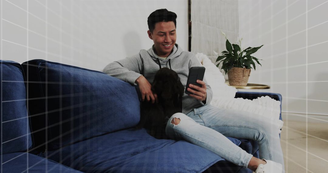 Smiling Man Relaxing on Blue Couch Using Smartphone While Petting Dog in Modern Living Room