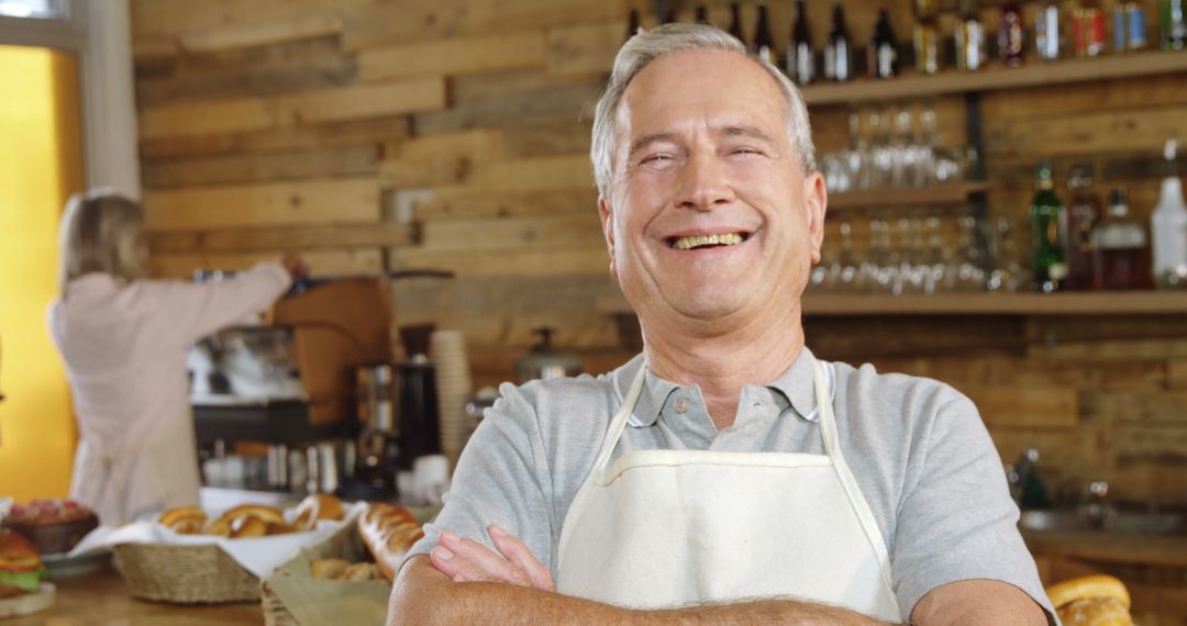 Smiling Senior Man in Cafe Wearing Apron with Arms Crossed - Free Images, Stock Photos and Pictures on Pikwizard.com