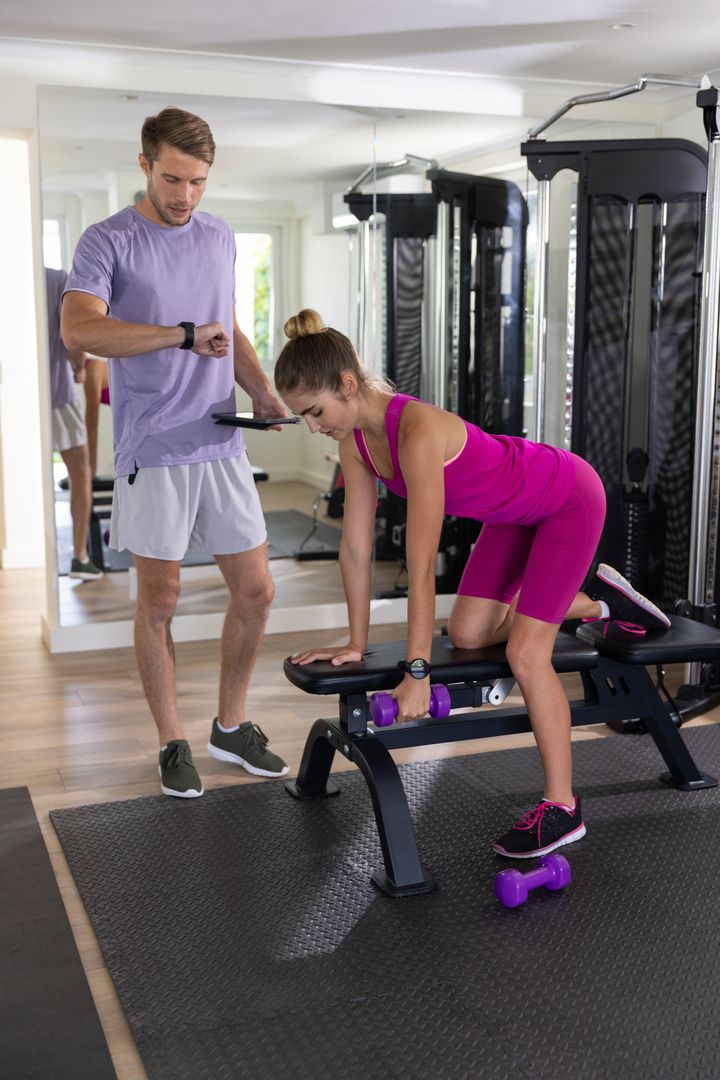 Personal Trainer Guiding Client Weightlifting with Dumbbell in Modern Gym