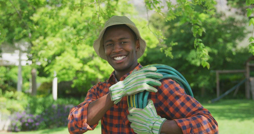 Young Man in Garden Holding Garden Hose and Smiling - Free Images, Stock Photos and Pictures on Pikwizard.com