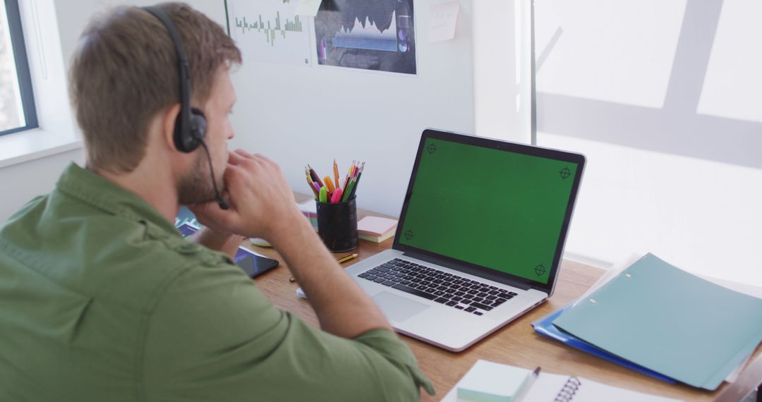 Man Wearing Headphones Working on Laptop with Green Screen at Home Office Desk - Free Images, Stock Photos and Pictures on Pikwizard.com