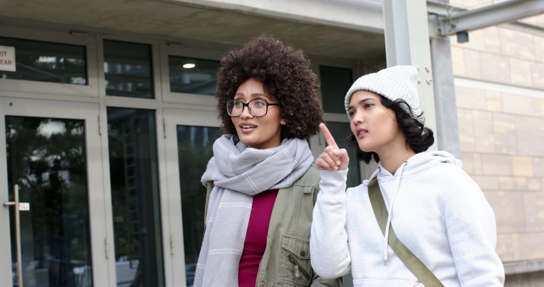 Two friends exploring campus entrance pointing direction, casual urban winter outfits