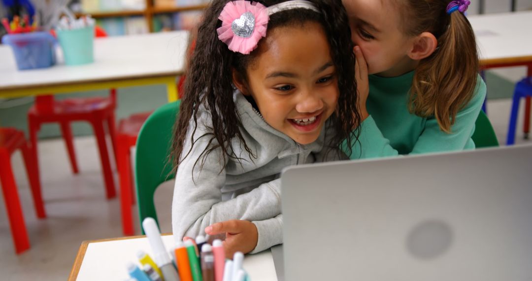Girls Whispering Secrets in Classroom Using Laptop