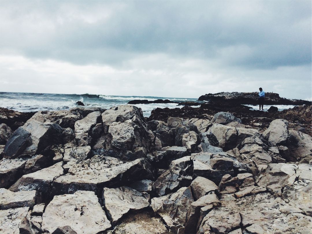 Rocky Shoreline with Cloudy Sky and Solitary Person - Free Images, Stock Photos and Pictures on Pikwizard.com