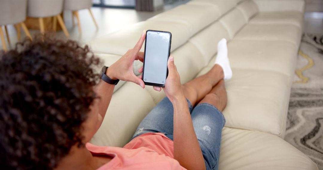 Young Man Relaxing on Sofa Using Smartphone at Home